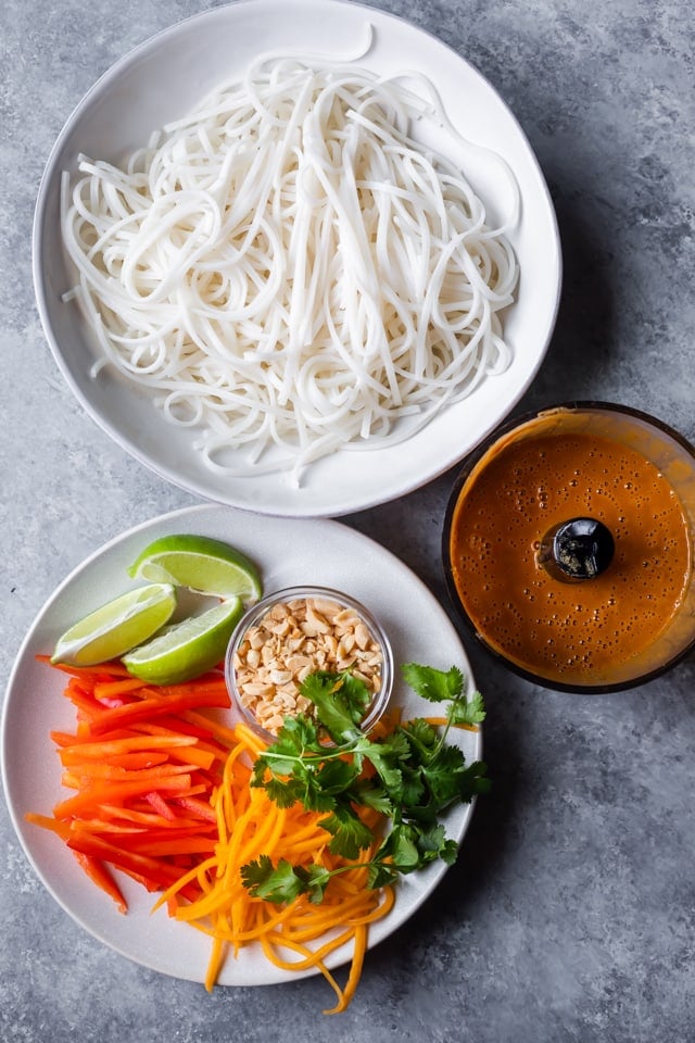 Ingredients to make asian noodle salad, including cooked rice noodles, vegetables and the creamy peanut dressing