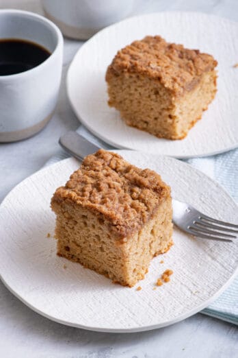 Two small plates of cinnamon coffee cake with coffee mug in background