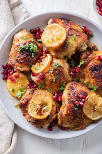 Close up shot of pomegranate roasted chicken thighs topped with lemon slices