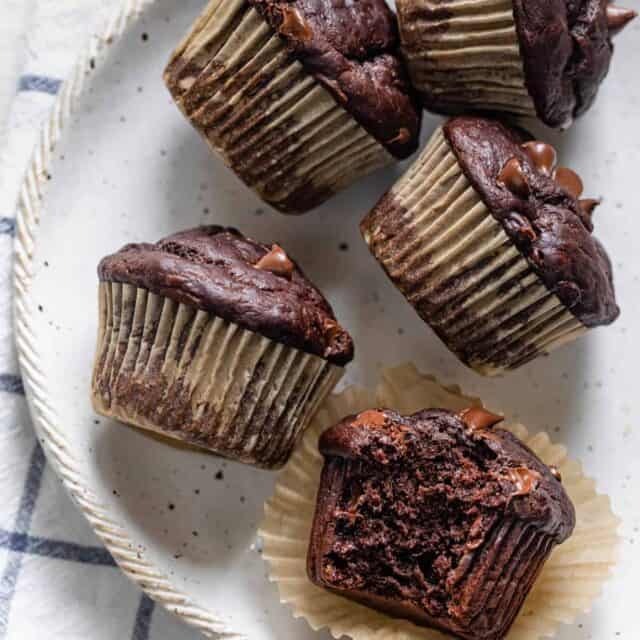 Chocolate banana muffins on a white plate with a bite taken out of one of them