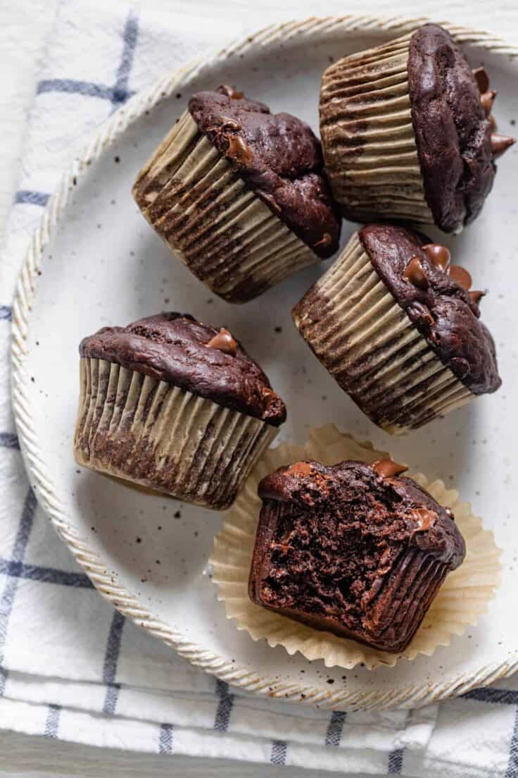 Chocolate banana muffins on a white plate with a bite taken out of one of them