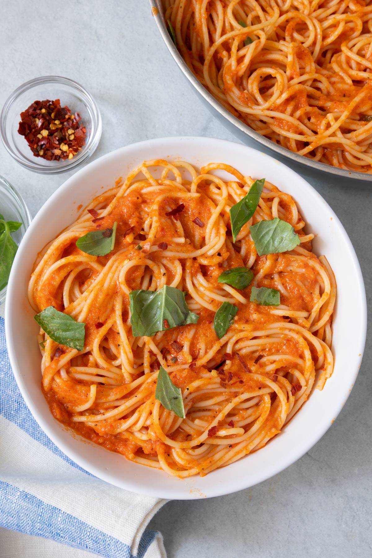 Bowl of creamy red pepper pasta next to skillet and side of red pepper flakes in small bowl.