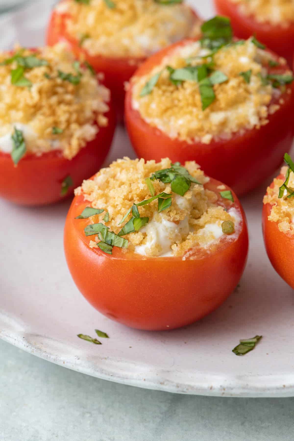 Stuffed tomatoes with fresh basil on plate with focus on one.