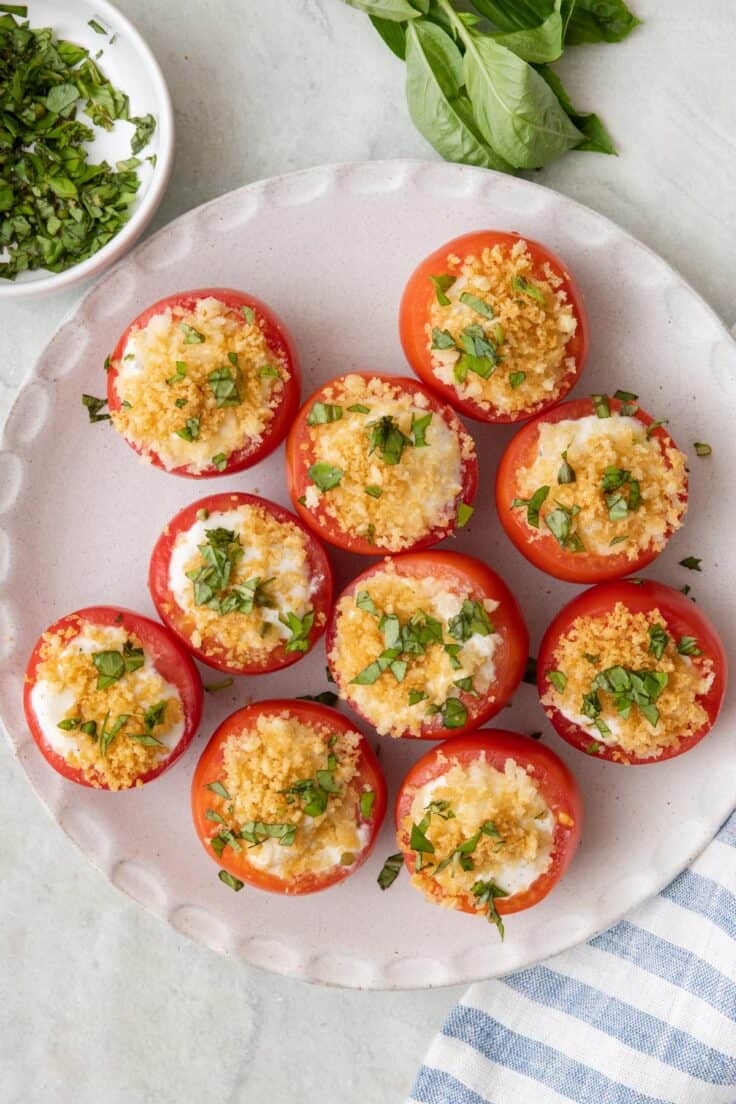 Tomatoes topped with toasted breadcrumbs and fresh basil on a serving dish.