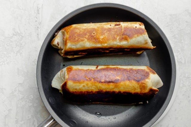 Two taco burritos rolled up on pan to cook the edges