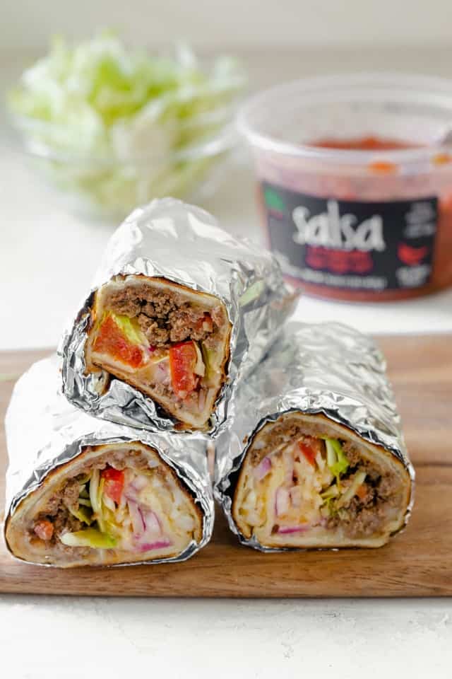 Three burritos stacked on top of each other with salsa in the background