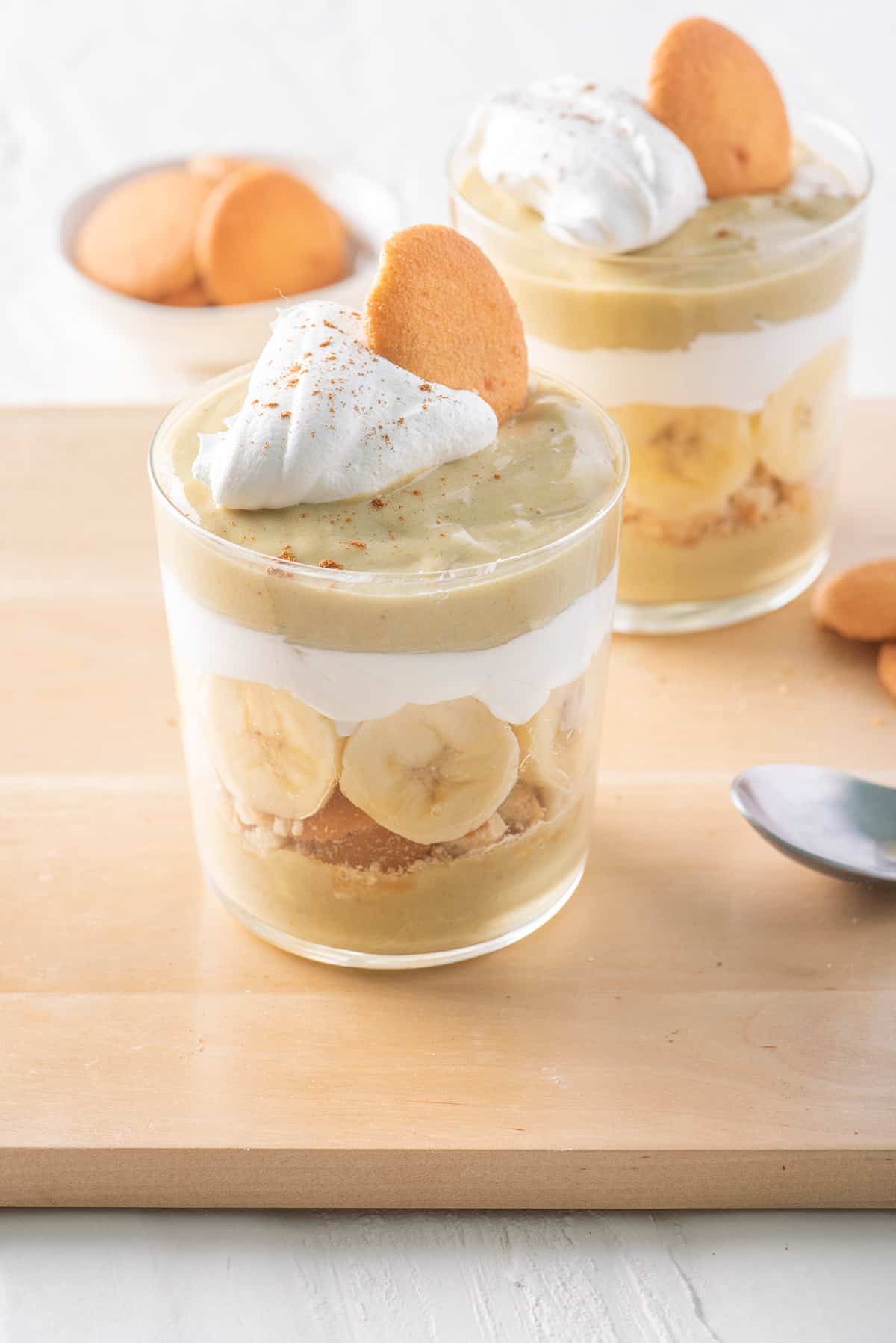 Two cups of banana pudding parfaits topped with whipped cream and wafer