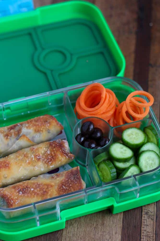green lunchbox with cucumbers spring rolls and carrots