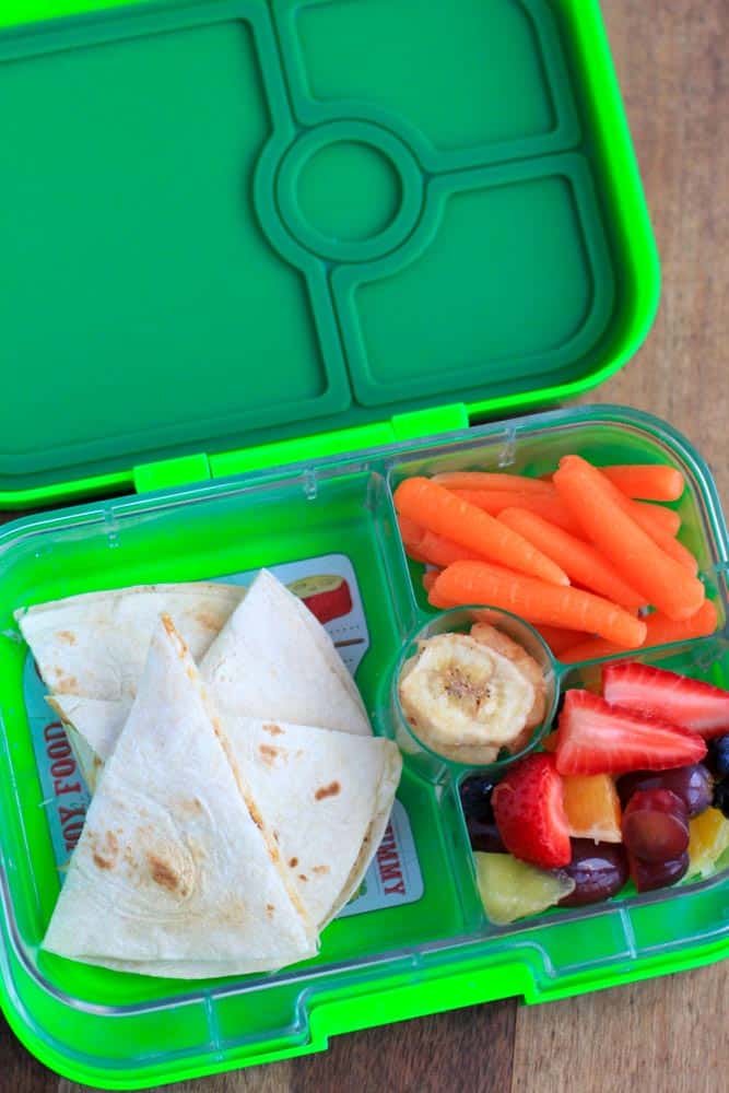 overhead shot of tortilla, fruit and carrots in a green lunchbox