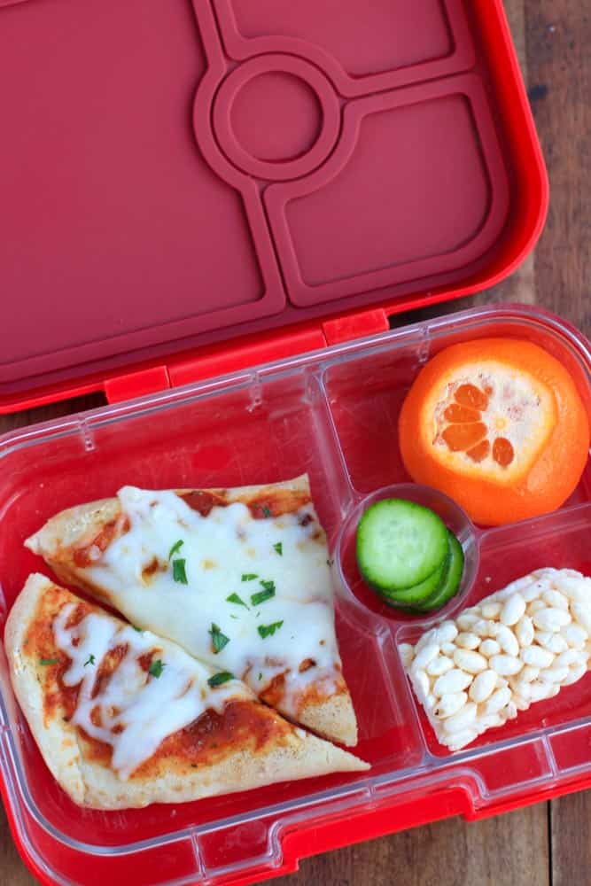 top down shot of red lunchbox containing slices of pizza and vegetables