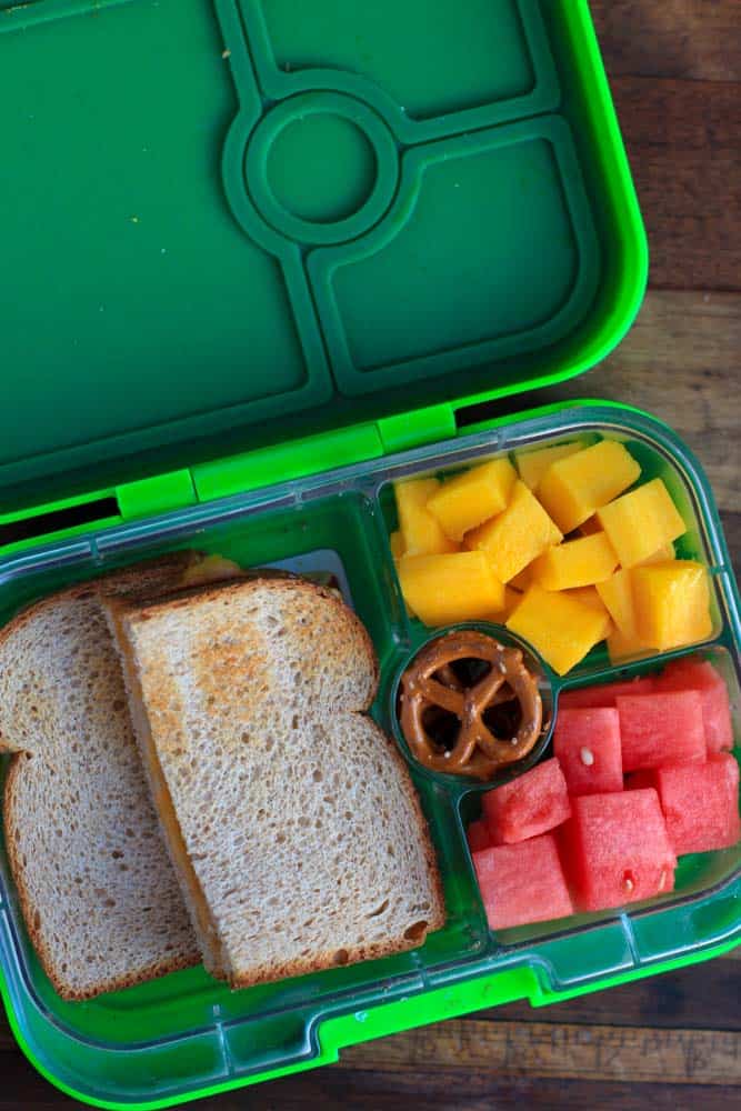 top down shot of green lunchbox containing a sandwich and fruit