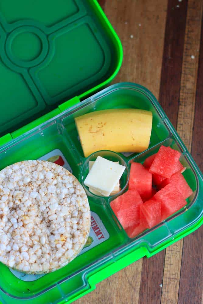 top down shot of green lunchbox with rice cracker and fruit