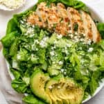 Large bowl of the green goddess salad topped with grilled chicken and avocado