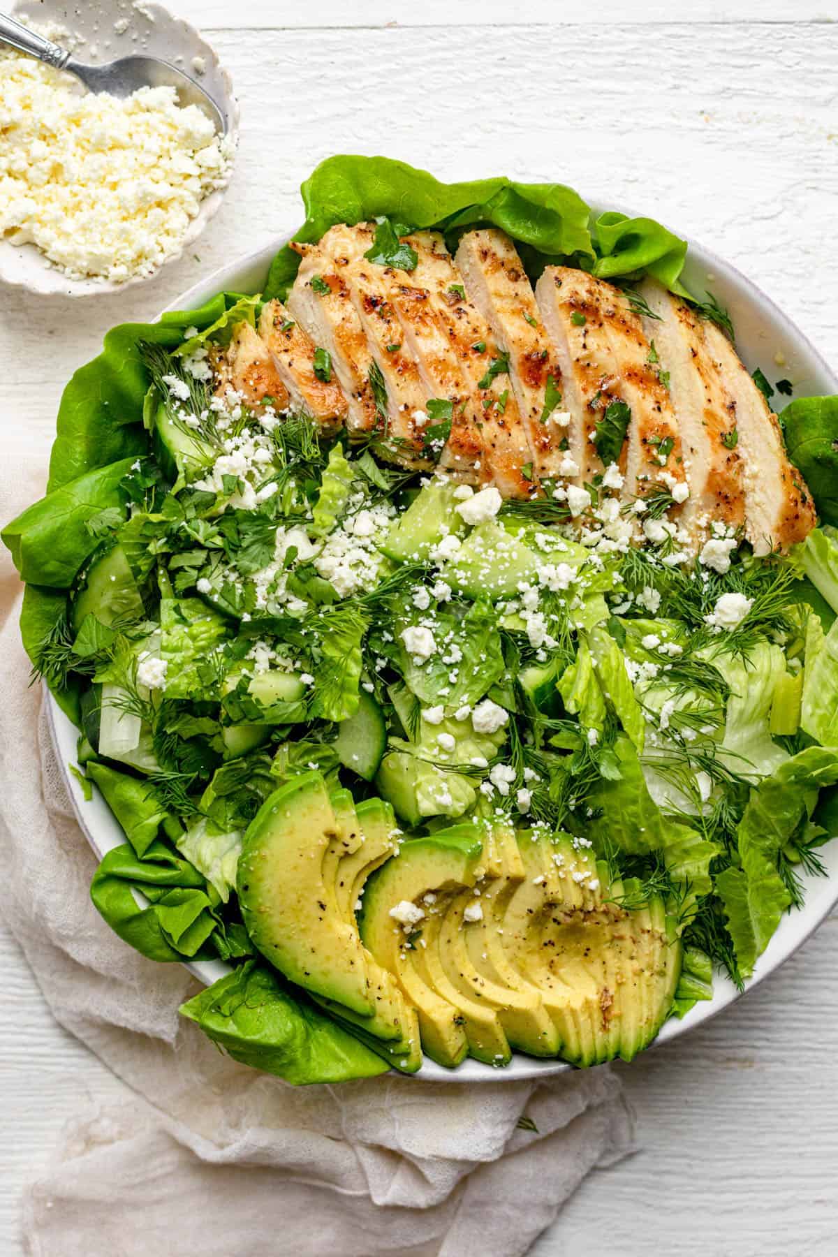 Large bowl of the green goddess salad topped with grilled chicken and avocado