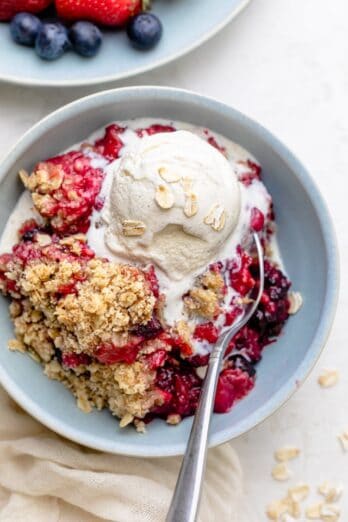 mixed berry crisp in a bowl with a scoop of ice cream