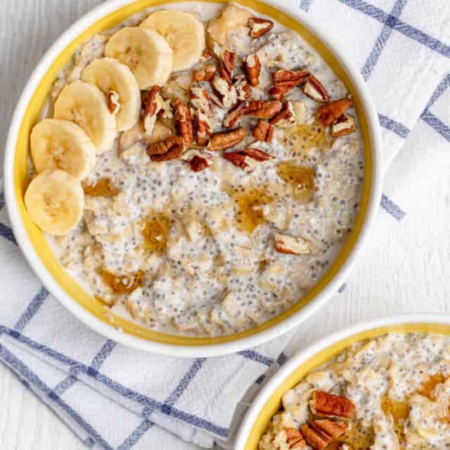 Top down view of two bowls with protein oatmeal topped with sliced bananas and pecans