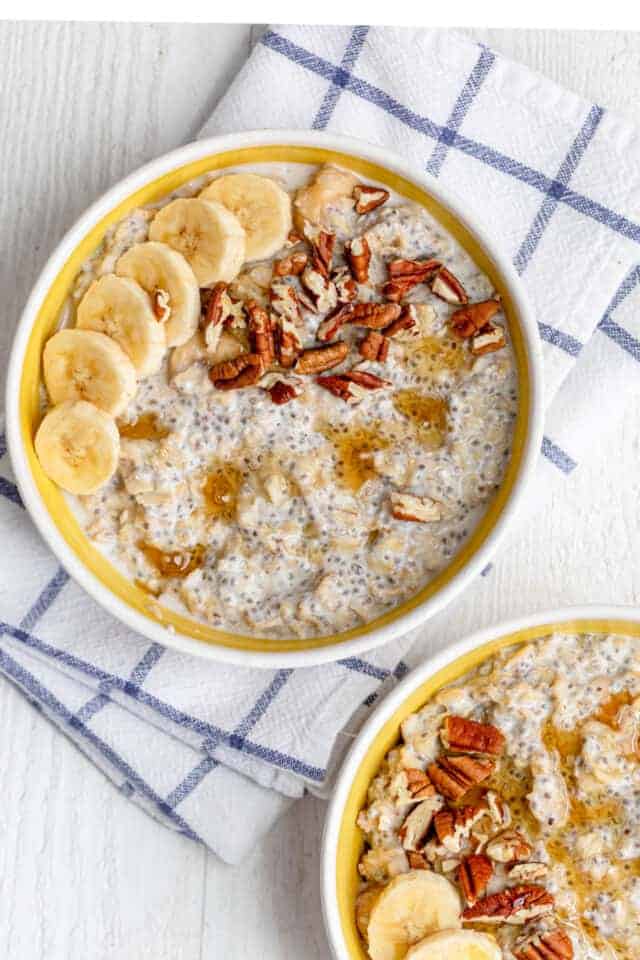 Top down view of two bowls with protein oatmeal topped with sliced bananas and pecans