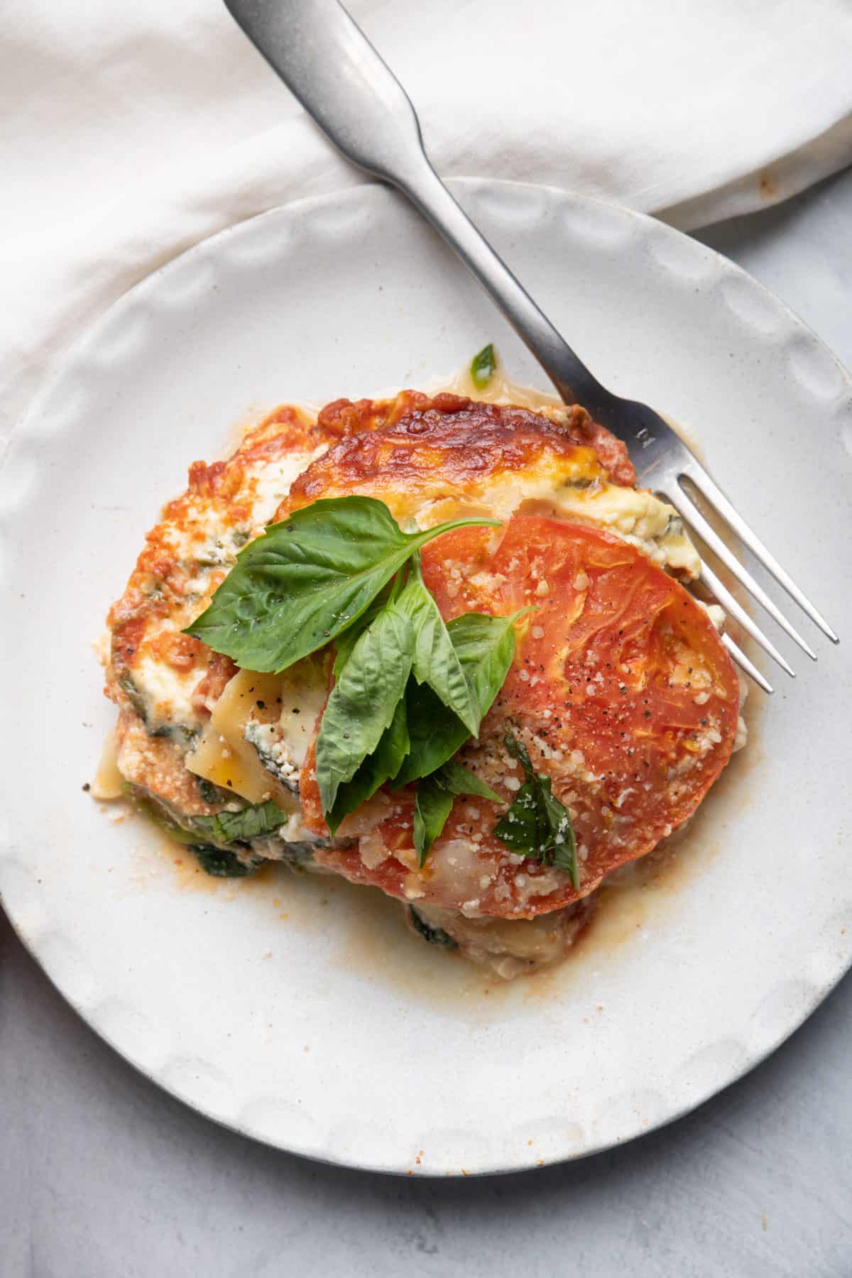 Plate with serving of tomato lasagna topped with basil