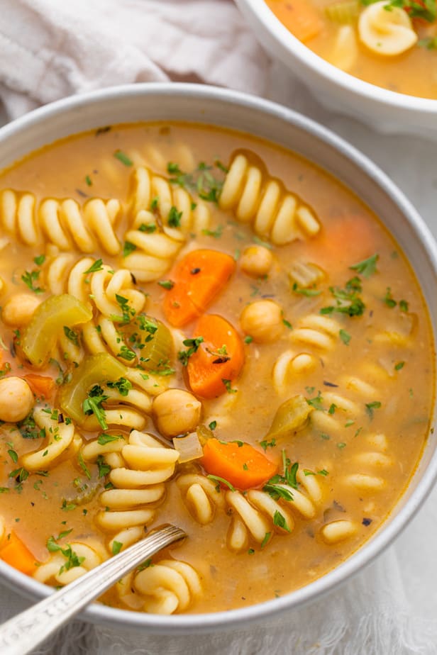 Close up shot of spoon inside large bowl of chickpea noodle woup