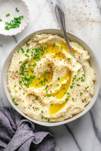 Large bowl of cauliflower mashed potatoes topped with melted butter and chives