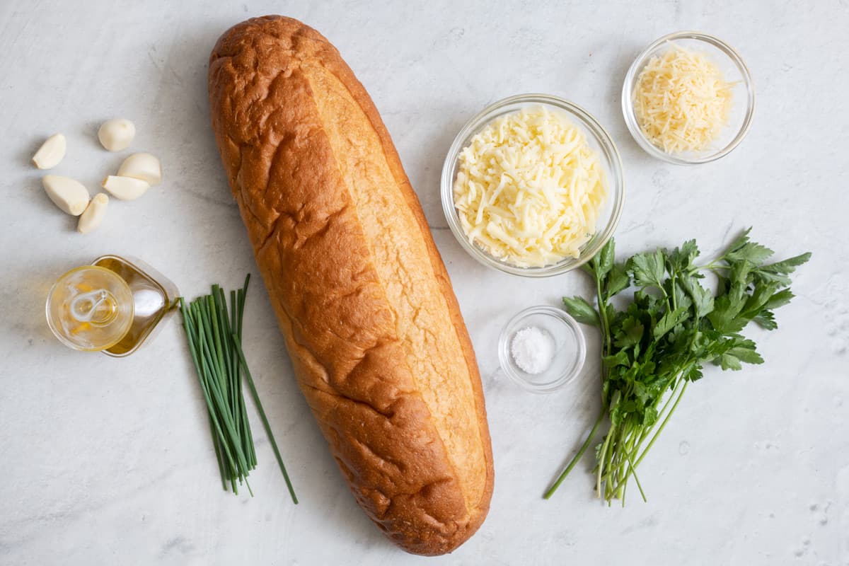 Ingredients for recipe: garlic cloves, oil, chive, 1 loaf of bread, shredded cheeses, salt, and fresh herbs.