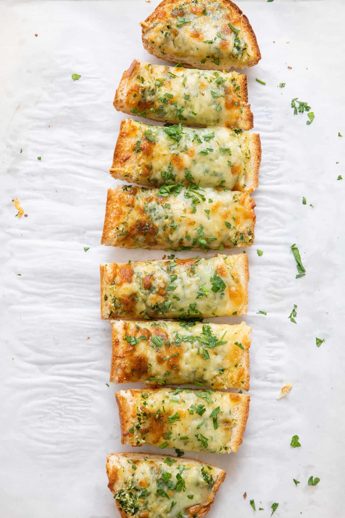 Sliced garlic bread on parchment paper with fresh parsley.