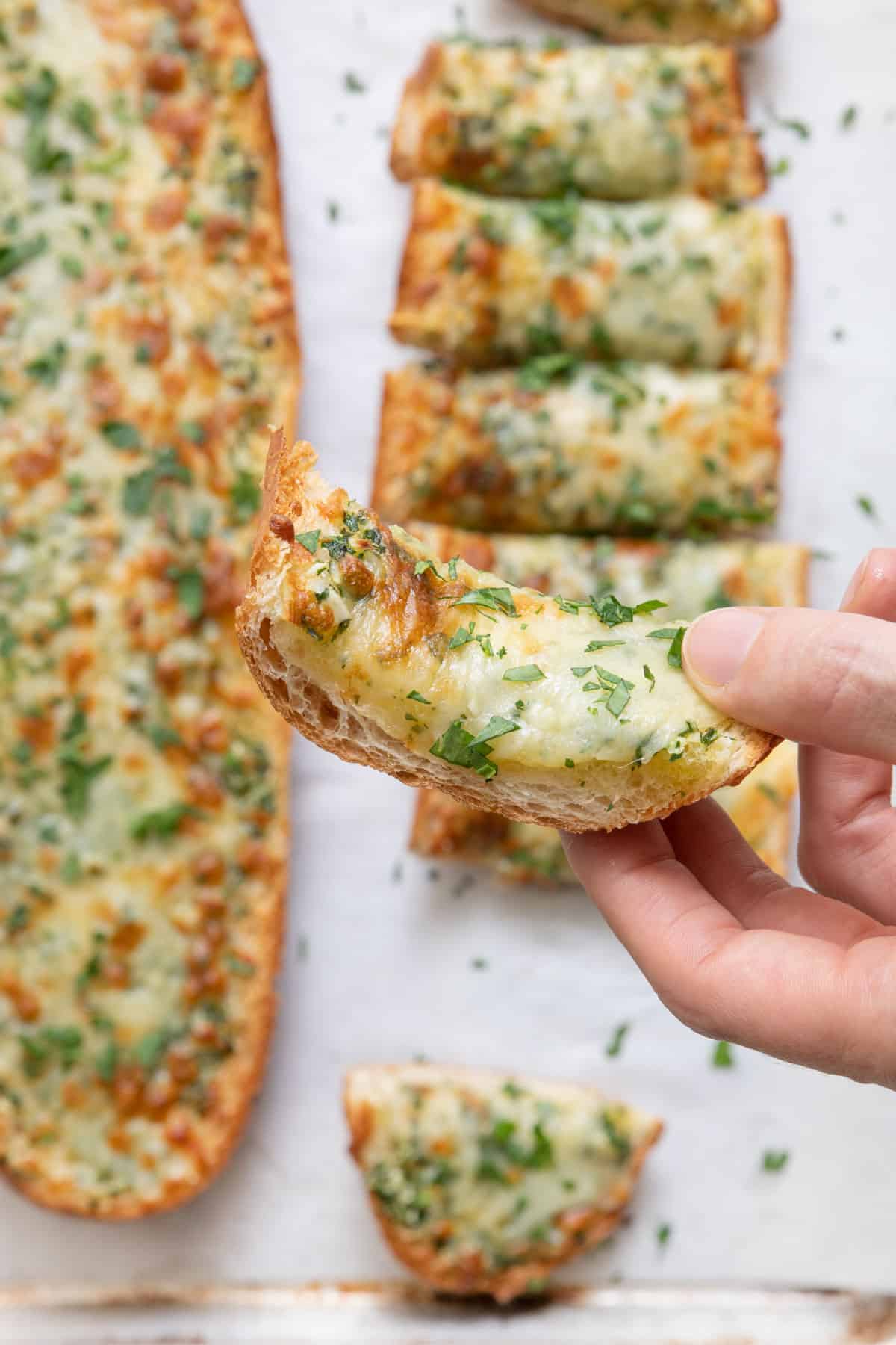 Hand hold a piece of garlic cheese bread with the loaf of bread shown below.