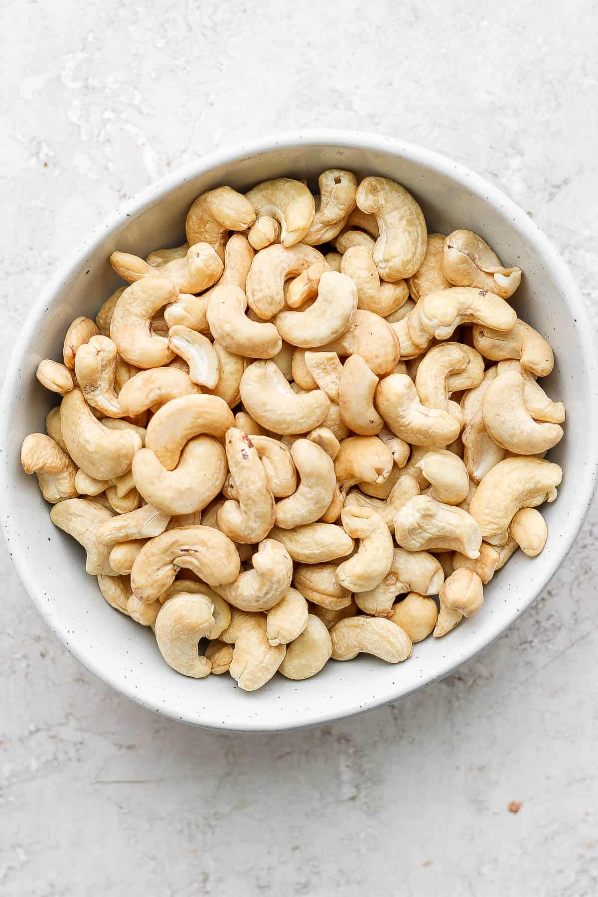 Raw cashews in a small white bowl with dark specks.