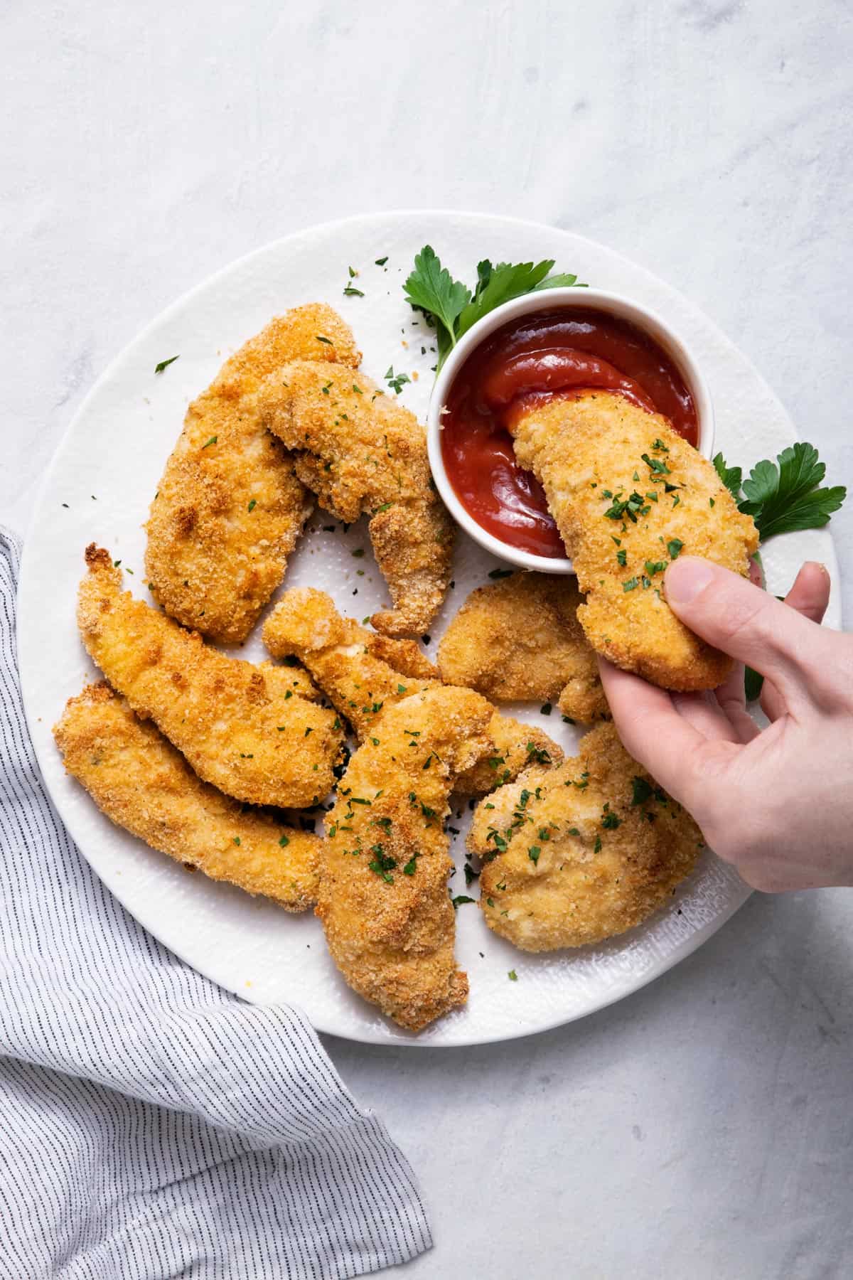 oven fried chicken tender dipping into ketchup