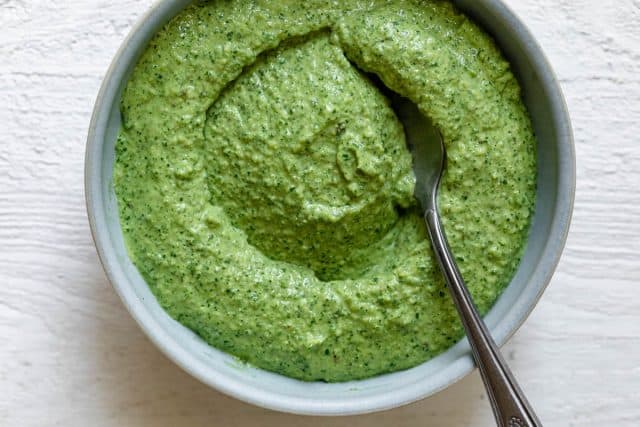Close up of pumpkin seed pesto sauce in a bowl with spoon inside