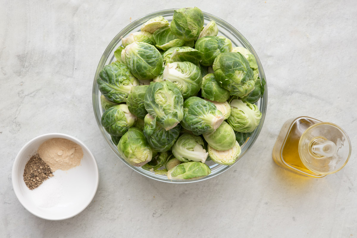 Ingredients for recipe: seasonings in a small dish, bowl of brussel sprouts, and oil.