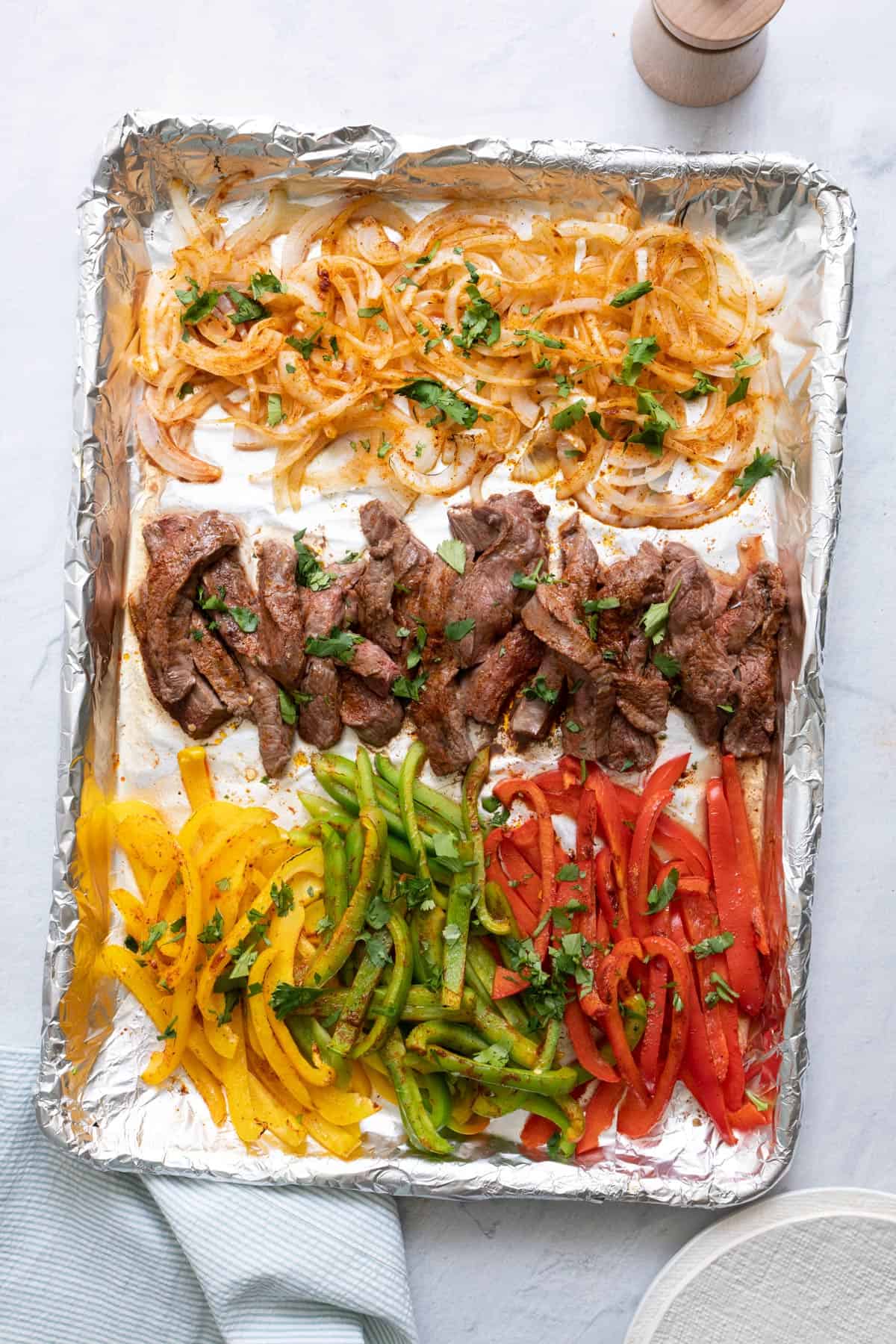 Sheet pan steak fajita ingredients baked and garnished with cilantro before combining.