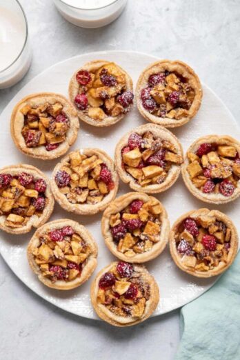 Mini cranberry apple pies on a white dish dusted with powdered sugar