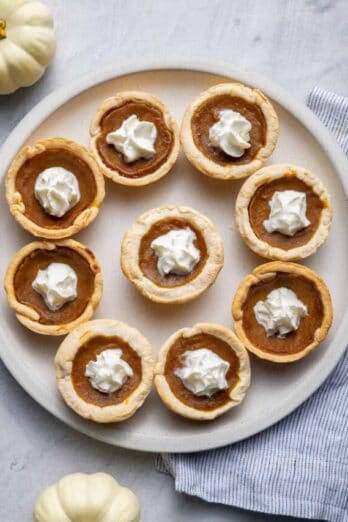 Mini pumpkin pies on a large plate with whipped cream in the middle