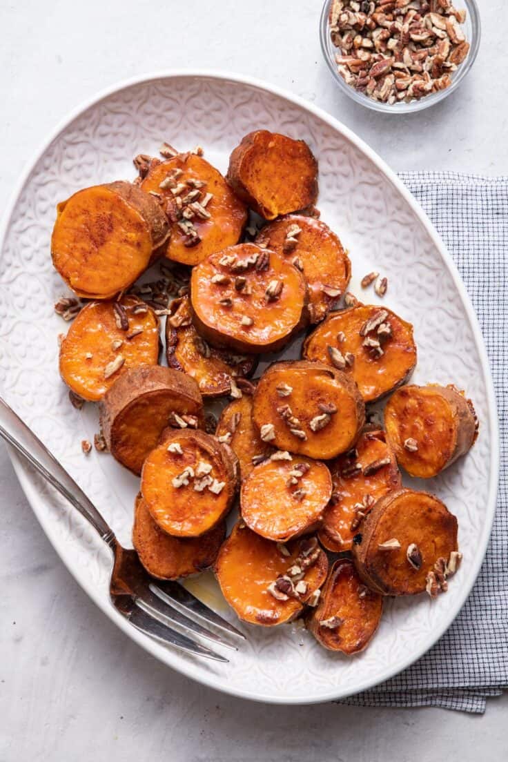 Large serving dish with melting sweet potatoes and pecans on the side