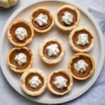 Mini pumpkin pies on a large plate with whipped cream in the middle