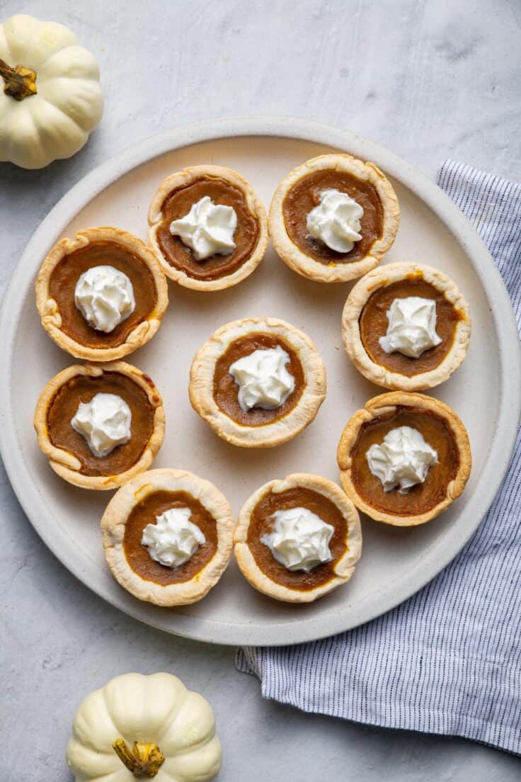 Mini pumpkin pies on a large plate with whipped cream in the middle