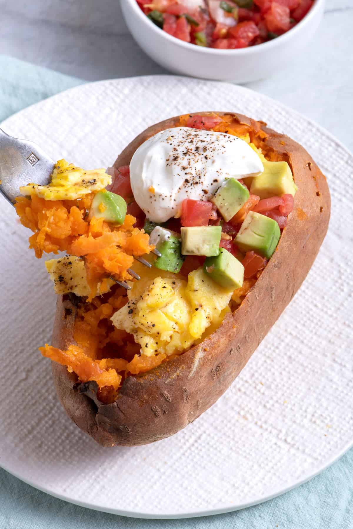 Fork digging into baked sweet potatoes loaded with eggs and veggies