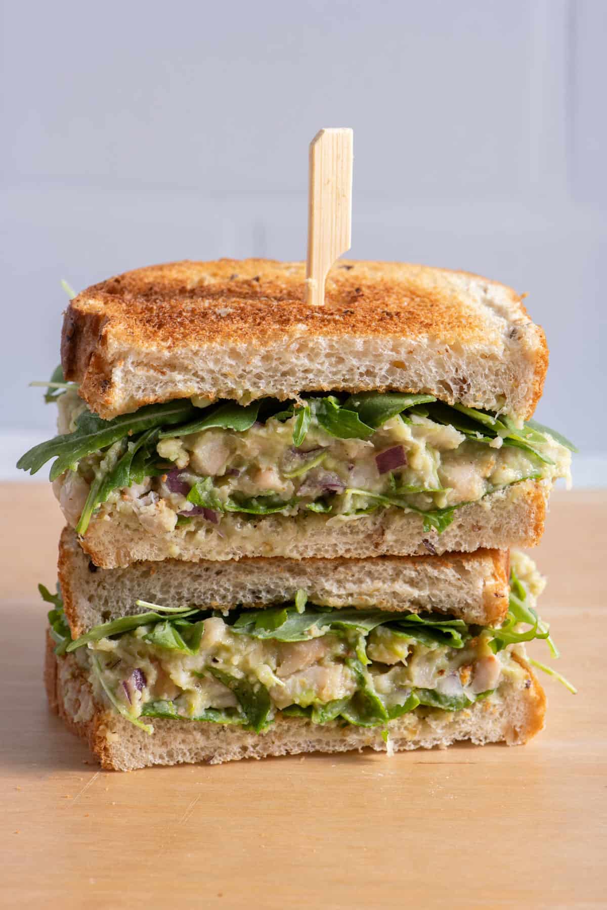 Stack of two halves of white bean avocado sandwich with toothpick holding them together