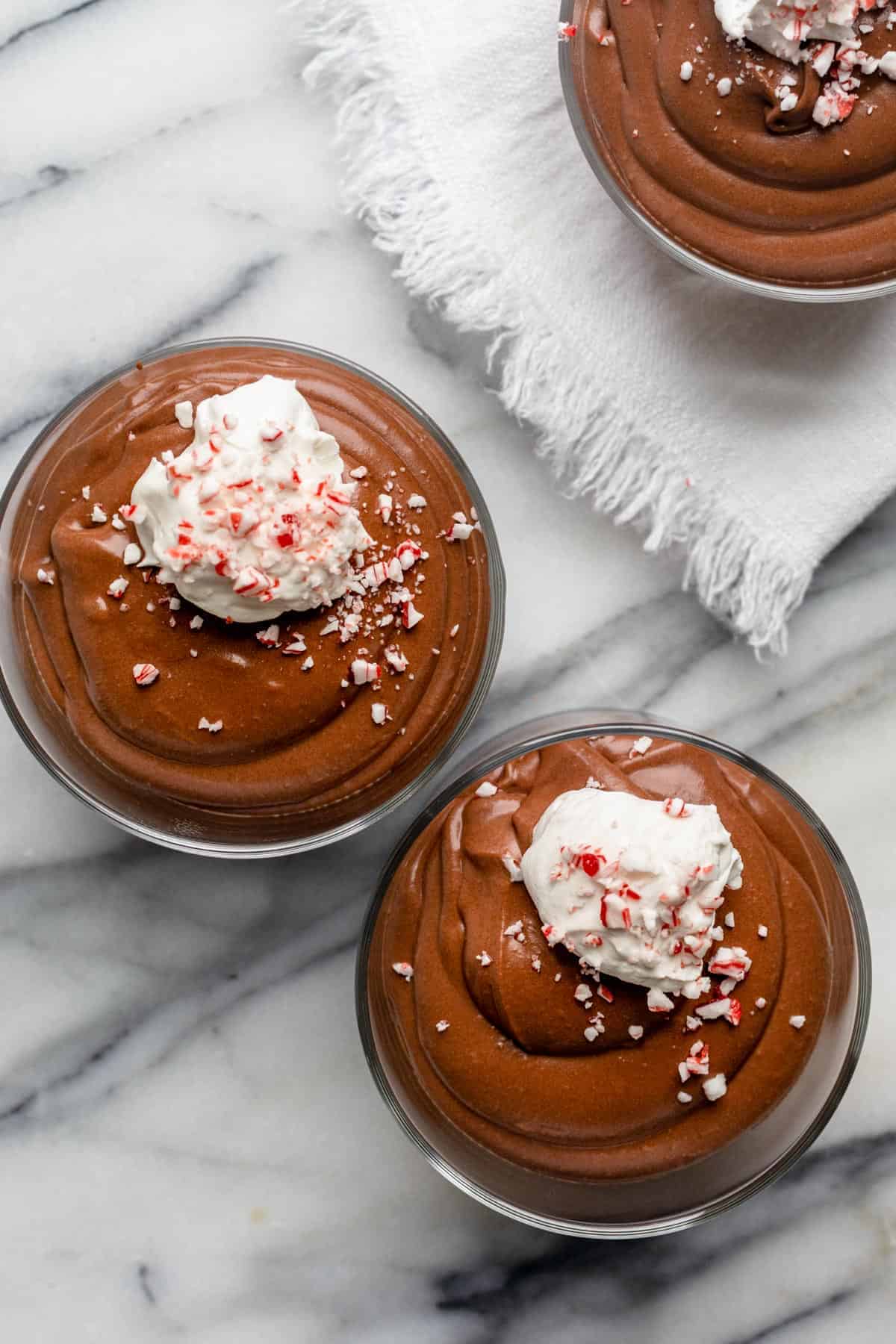 Three small bowls of chocolate peppermint mousse topped with cream and peppermint