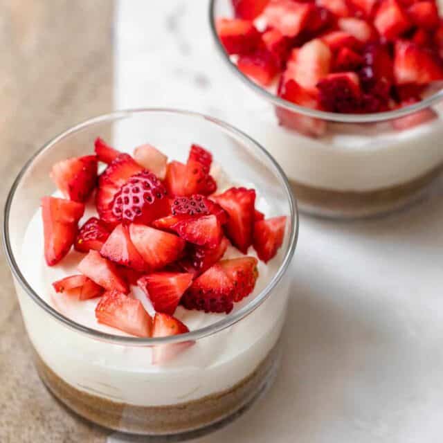 Greek Yogurt Cheesecake in two small clear glass bowls topped with strawberries
