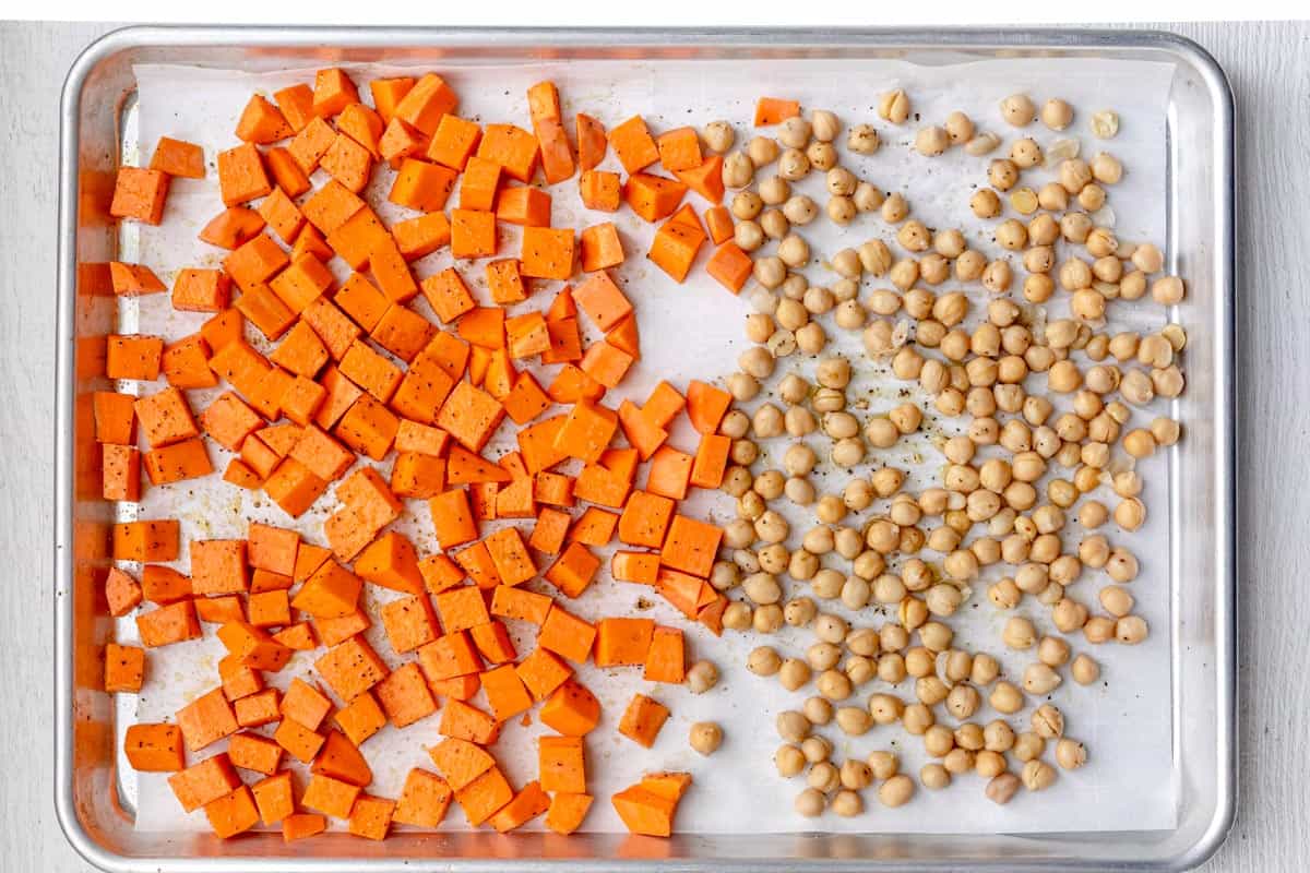 Cubed sweet potatoes and dried chickpeas on a baking dish lined with parchment paper