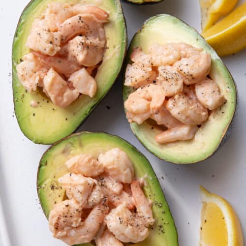 Plate with 4 avocado halves with shrimp cocktail inside each and lemon wedges on the side