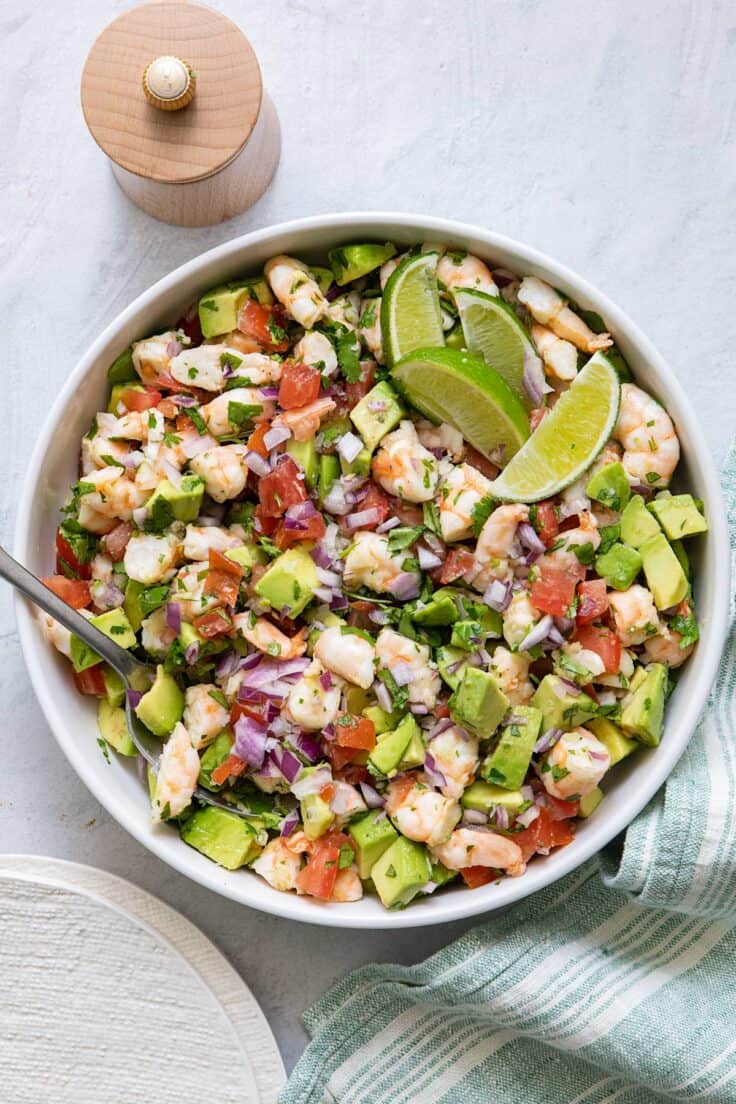 Overhead image of shrimp salad with avocado garnished with lime slices.