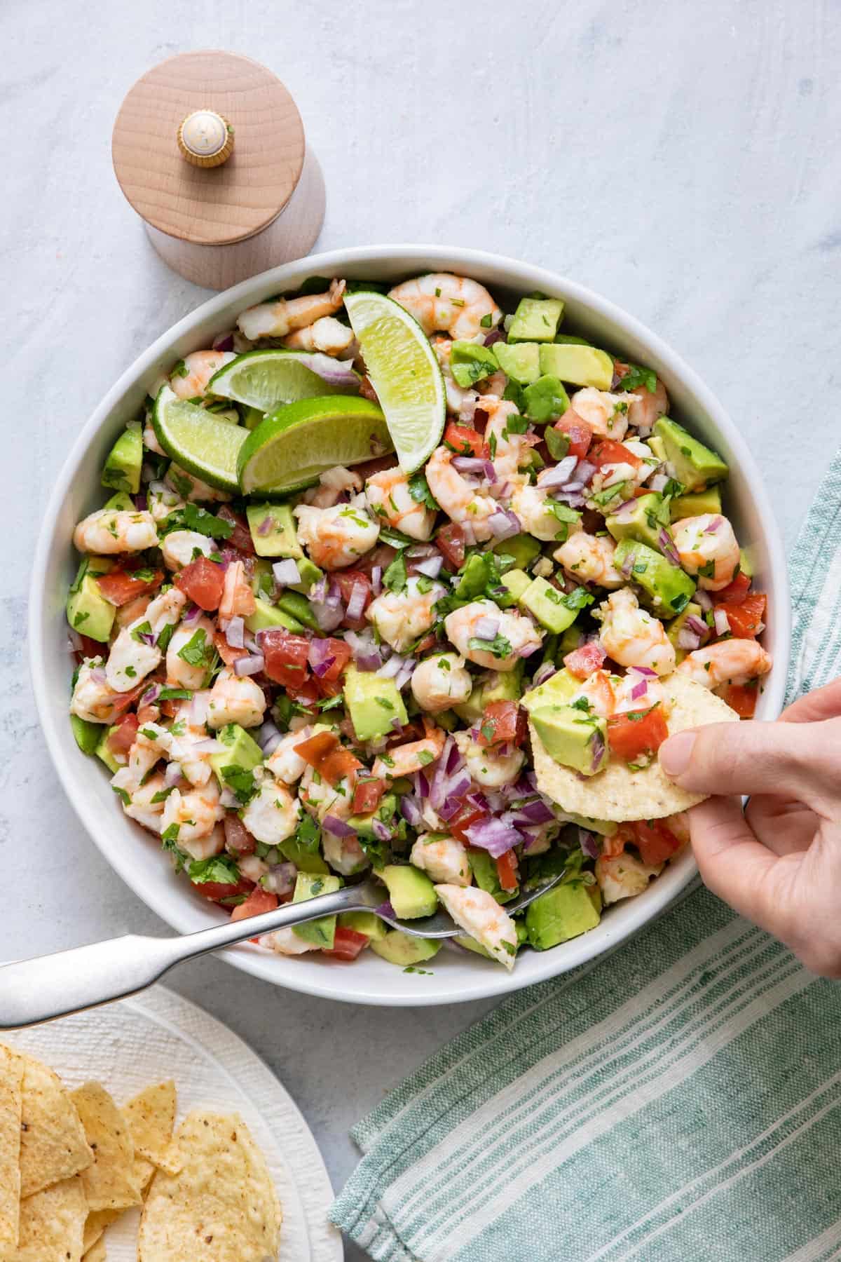 Large serving bowl of Shrimp avocado salsa with hand taking out a bite on a tortilla chip.