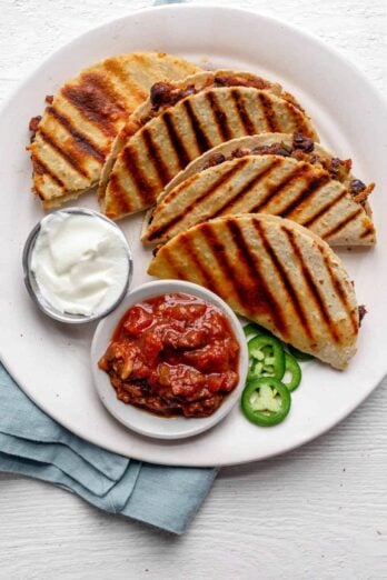 4 small bean and cheese quesadillas on a plate served with sour cream and salsa