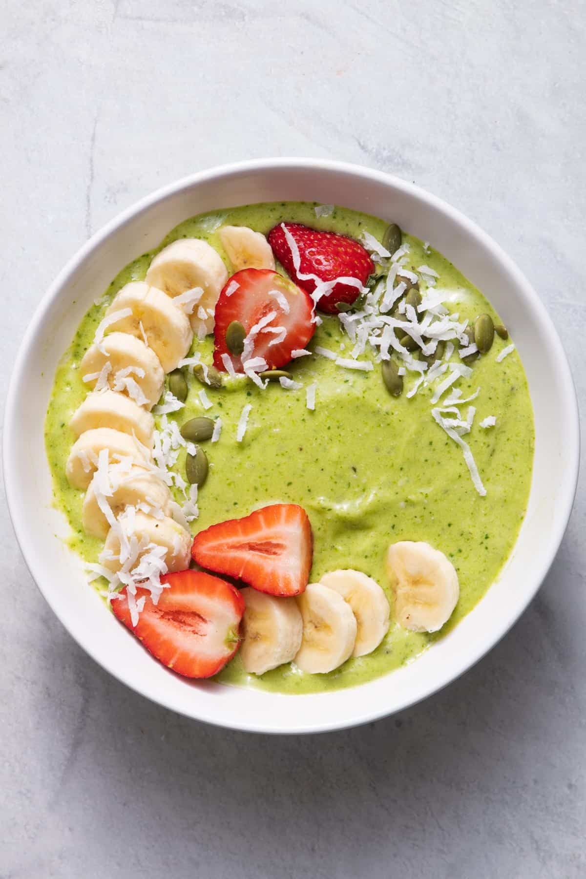 Sweet green smoothie bowl topped with fresh fruit