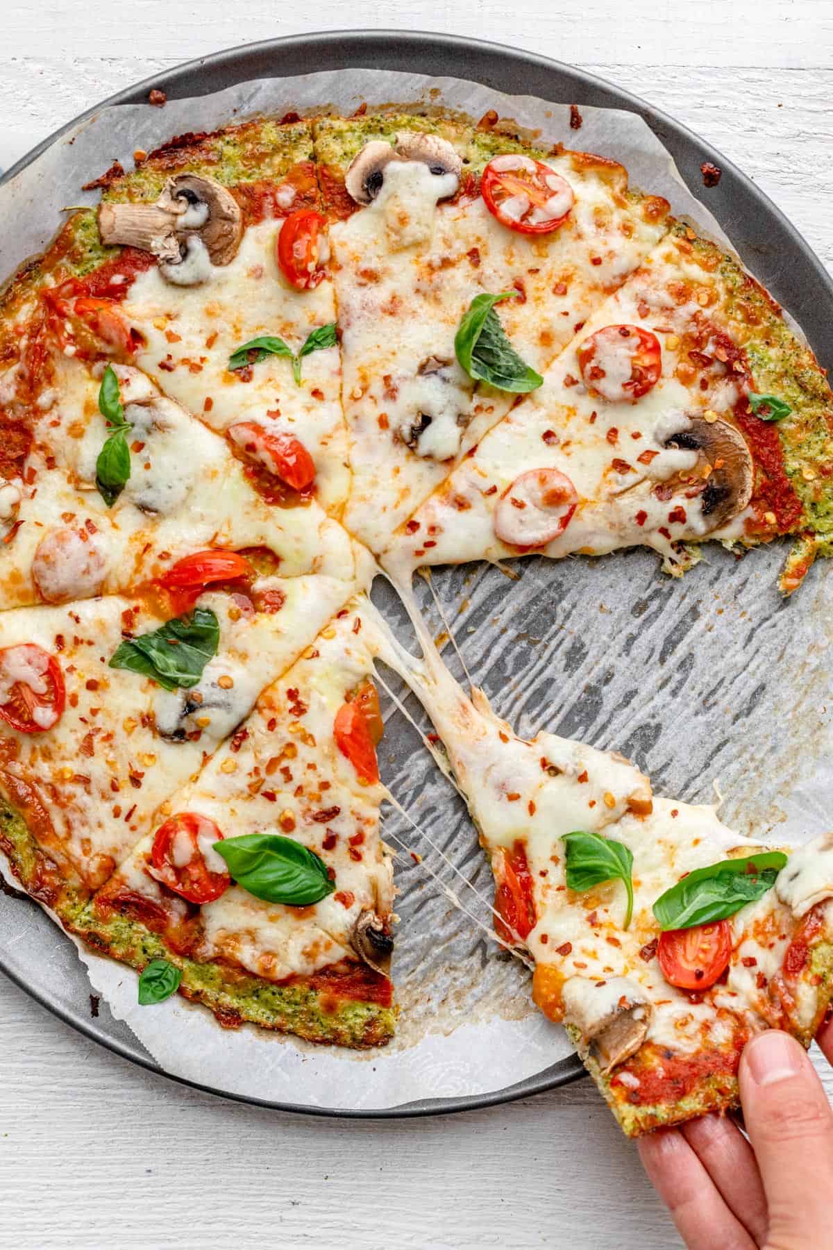 Pulling slice of broccoli pizza to show the cheesy bite