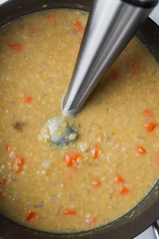 Immersion blender inside pot of crushed lentil soup right before blending