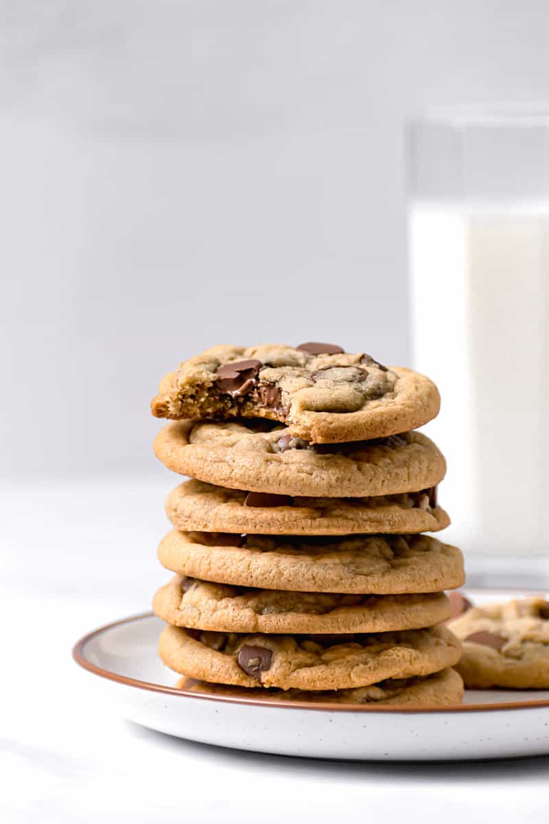 Stack of chocolate chip cookies on a plate with glass of milk in the background